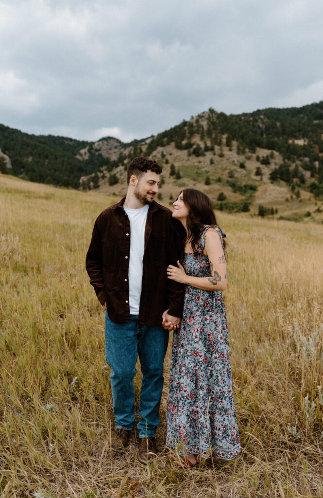 Couple smiling at each other in a field during engagement session in Boulder, CO