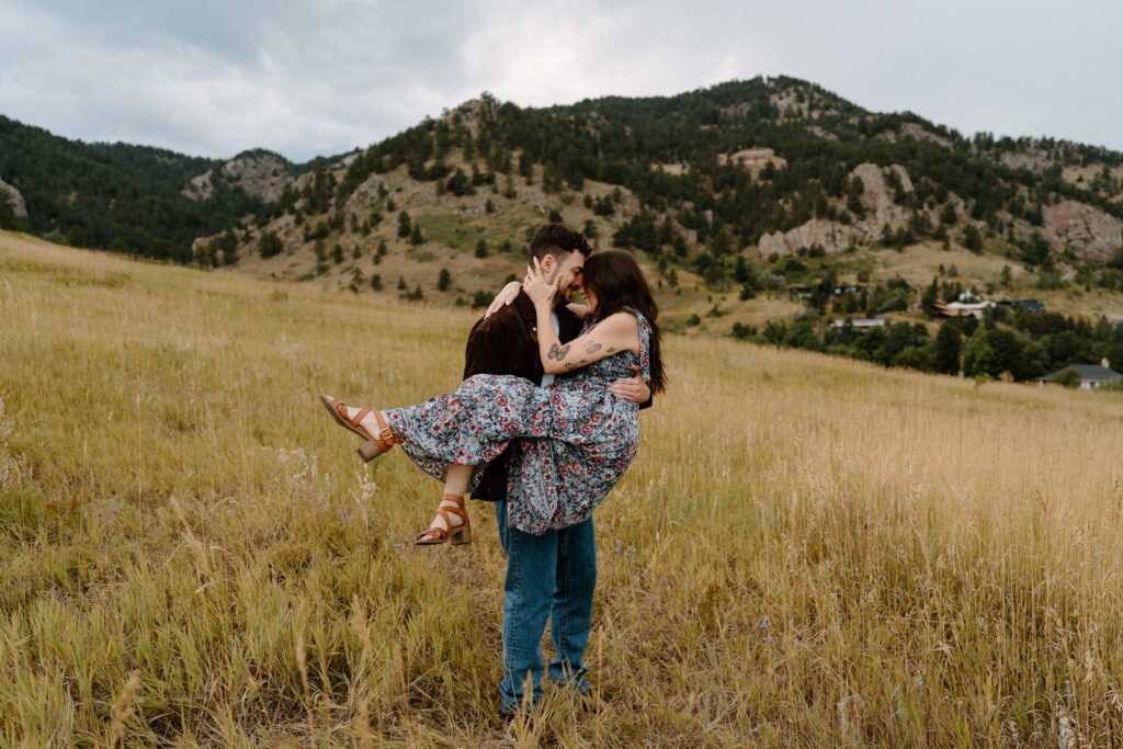 Fiancé holding fiancée in a field during an engagement session in Boulder, CO