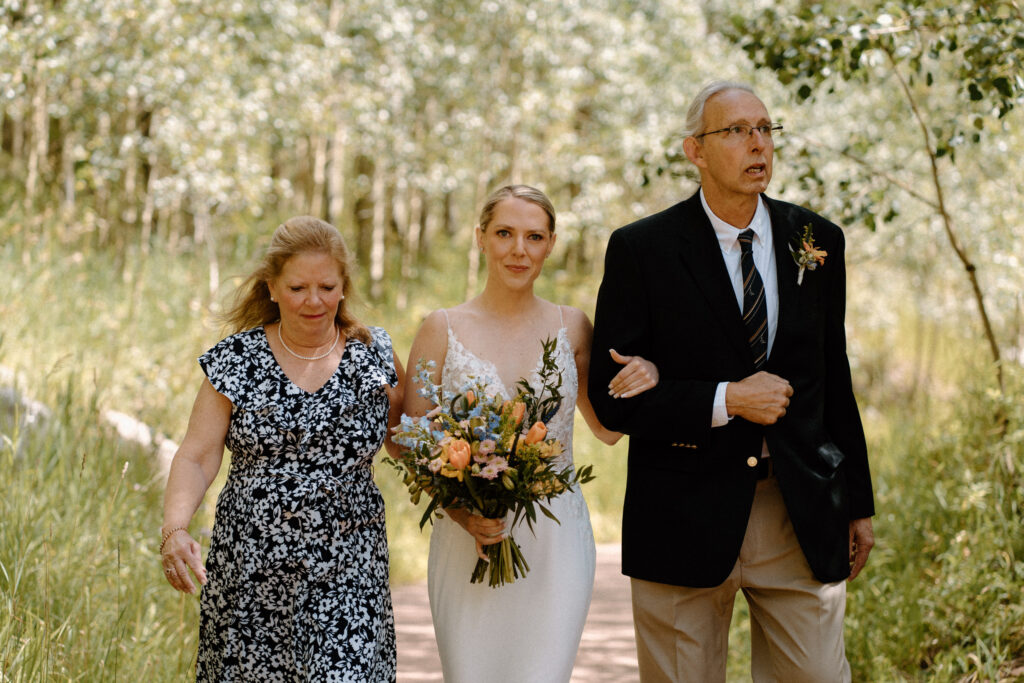 Bride and parents smiling while walking down the aisle during an elopement at Maroon Bells