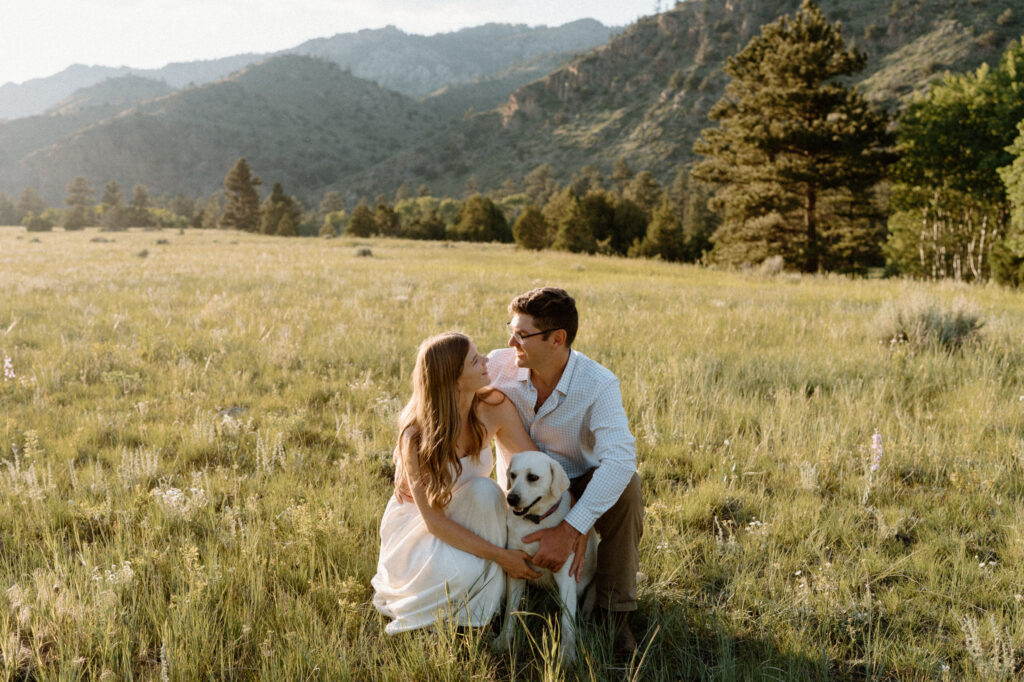 Couple smiling while playing with dog during engagement session at Poudre Canyon