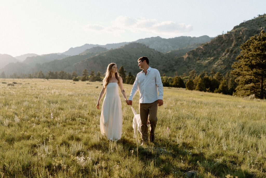 Couple holding hands and walking with dog during engagement session at Poudre Canyon