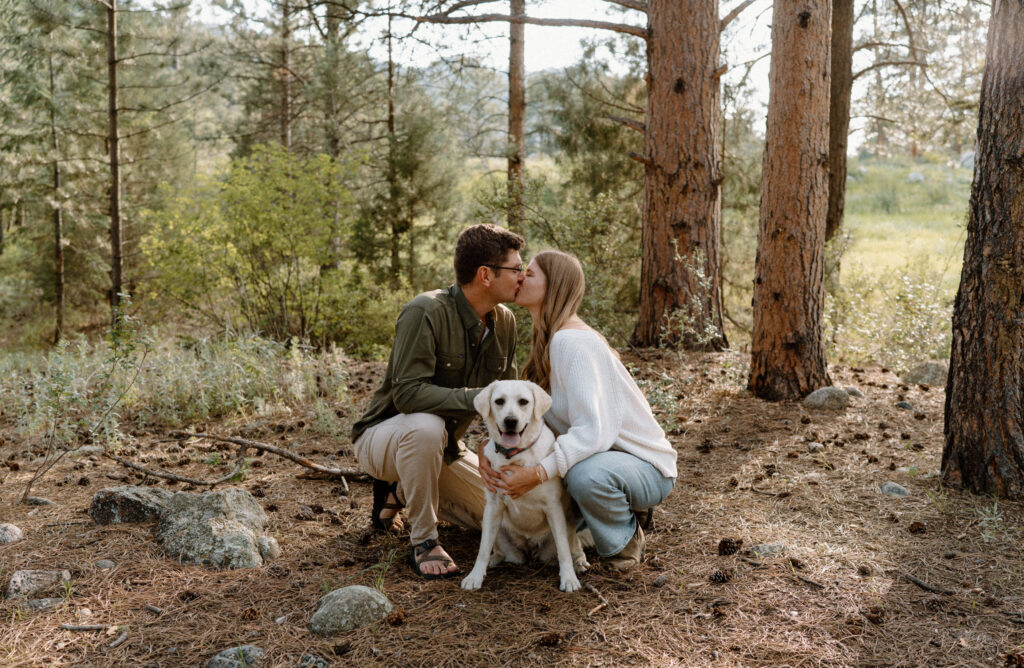 Couple kissing while holding dog during engagement session at Poudre Canyon