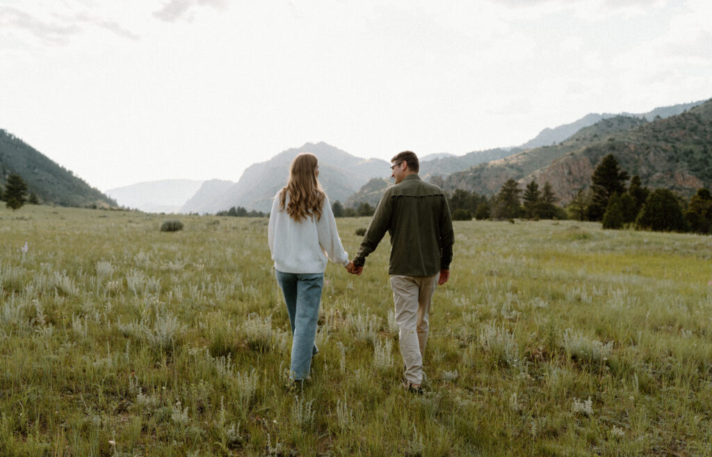 Couple holding hands in a field during engagement session at Poudre Canyon
