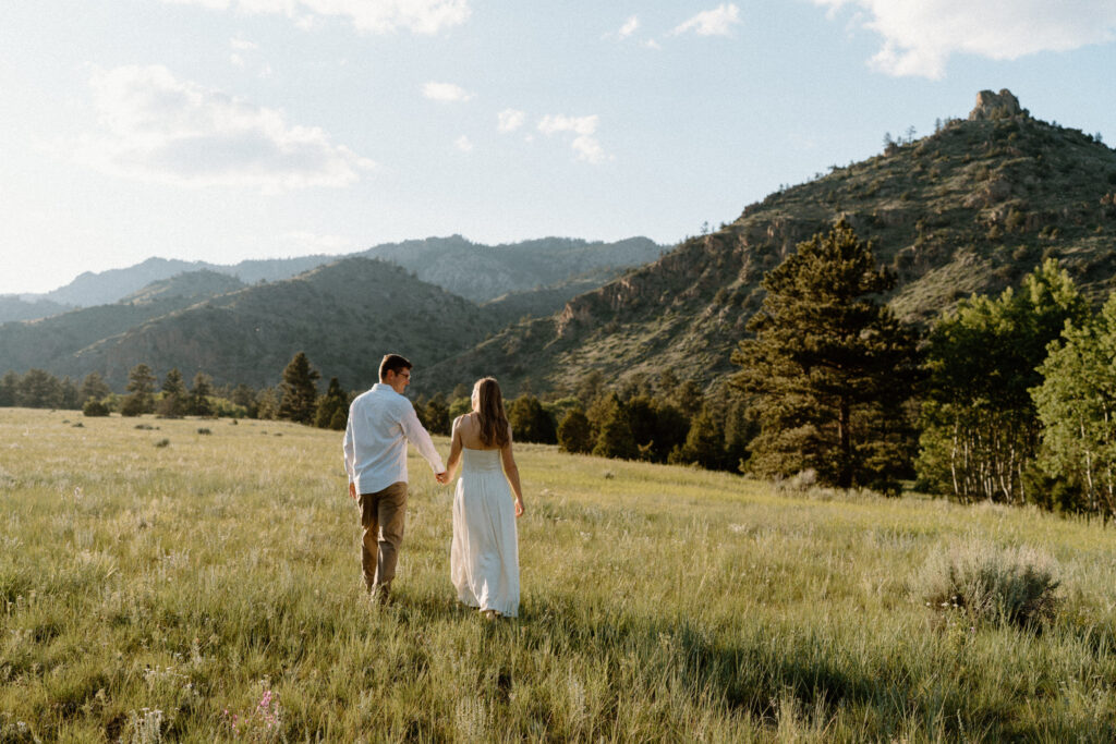 Couple walking in a field during an engagement session during Poudre Canyon