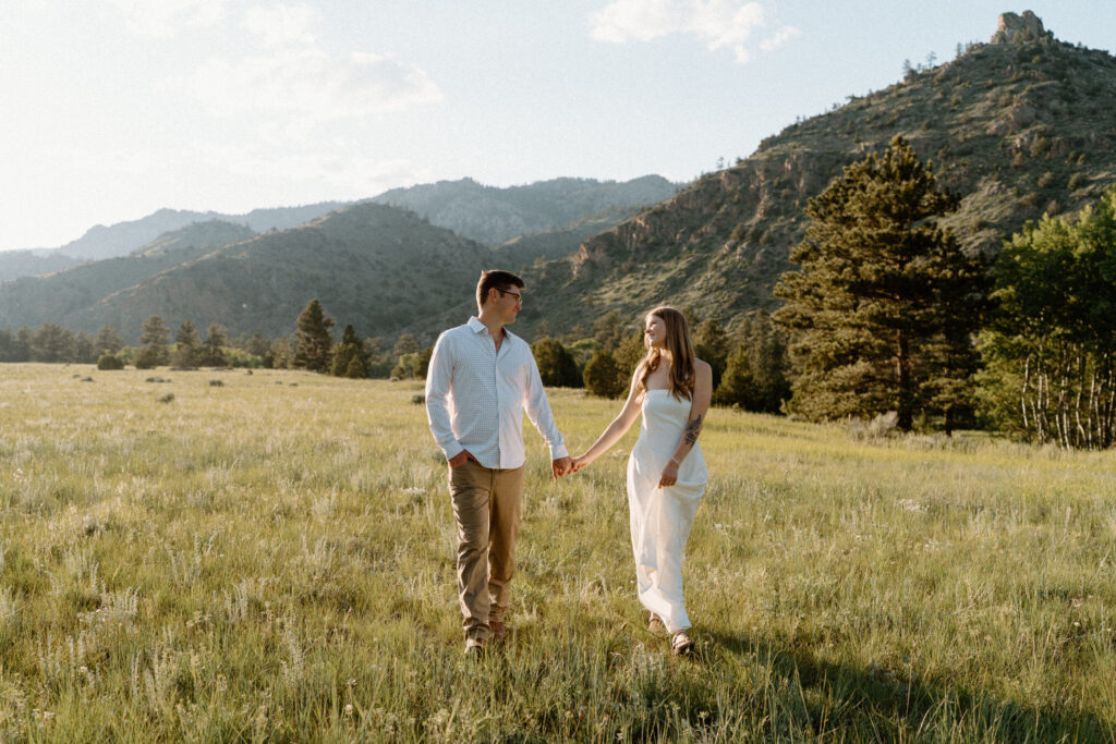 Couple holding hands and walking in a field during an engagement session at Poudre Canyon
