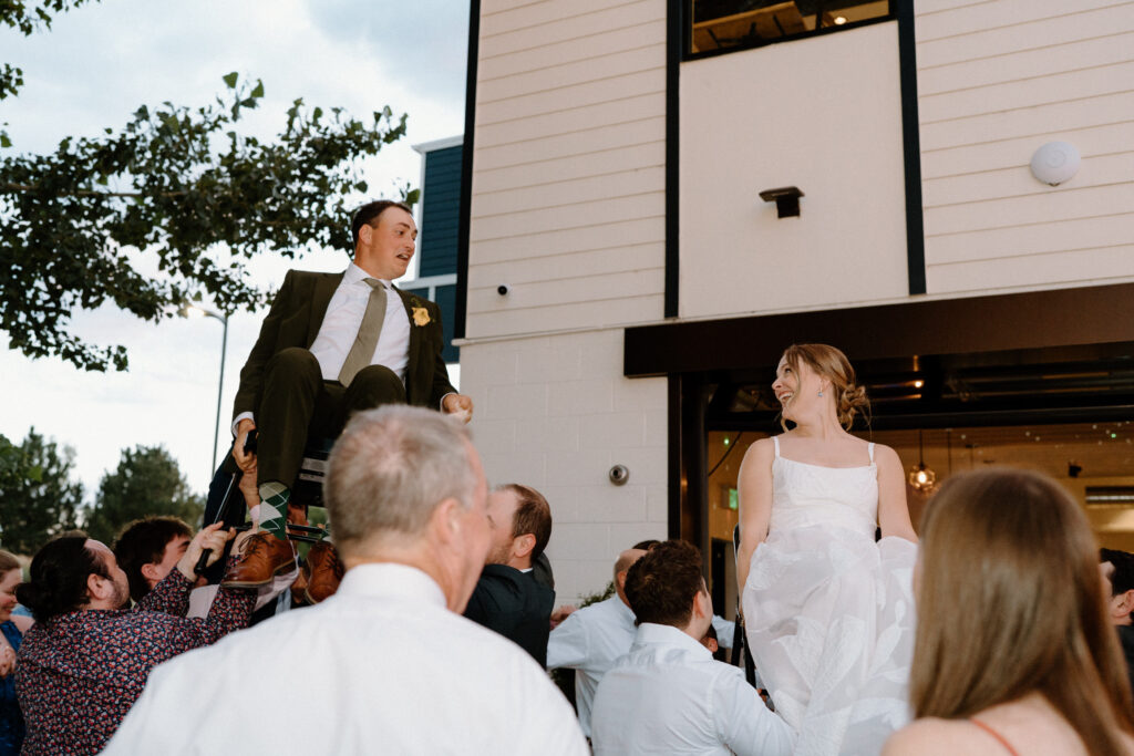 Bride and groom being carried on chairs on wedding day at Mountain Crust