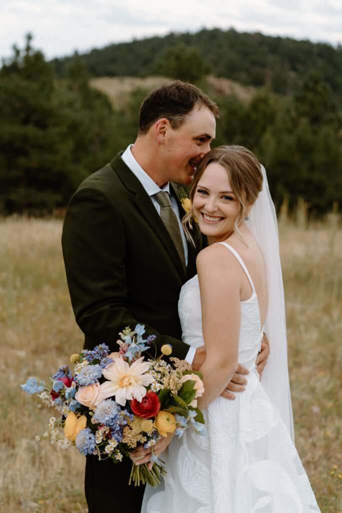Groom laughing in bride's ear on wedding day at Mt. Falcon