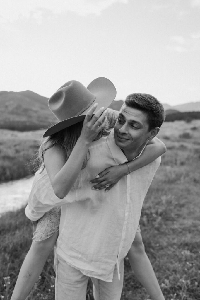 Couple smiling at each other while fiancée is on fiancés back during an engagement session at Rocky Mountain National Park
