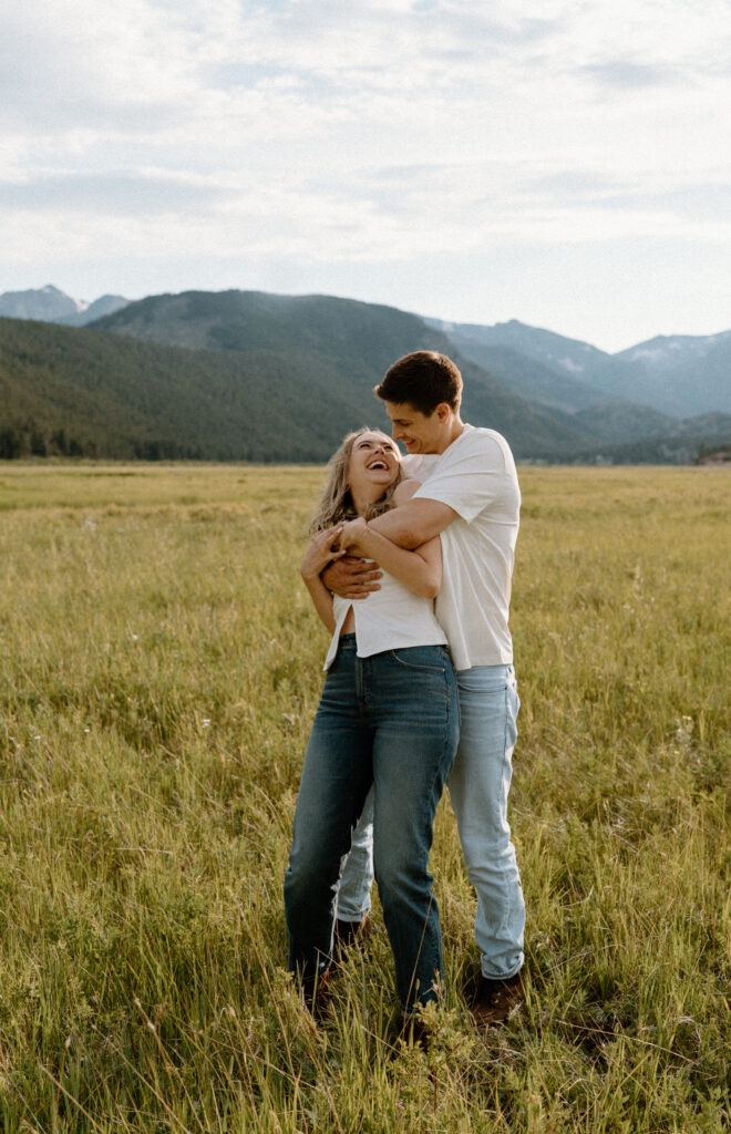 Couple laughing and smiling in a field at Rocky Mountain National Park during an engagement session