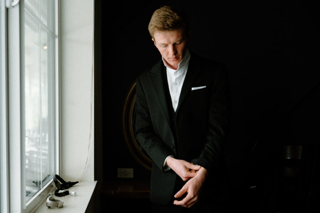 Groom putting on suit jacket on wedding day at Woodlands