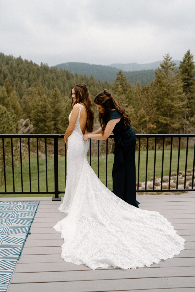 Bridesmaid helping bride into her dress on wedding day at Woodlands