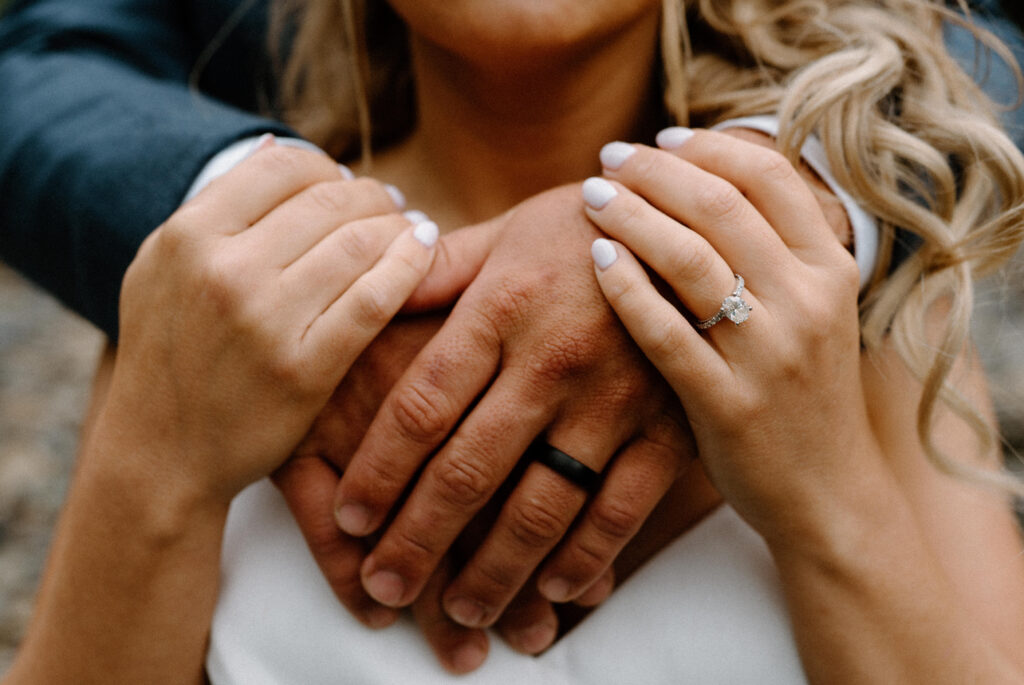 Groom hugging bride showing wedding bands during an elopement in Glacier National Park