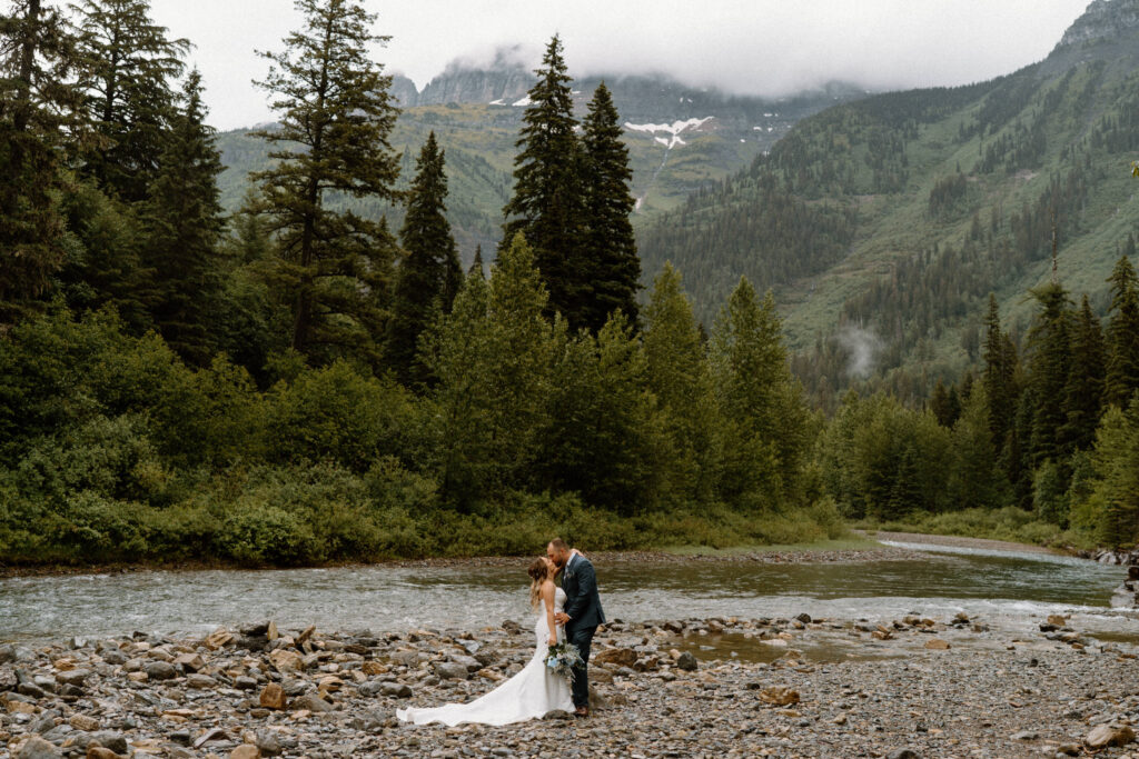 Bride and groom kissing near a river during an elopement in Glacier National Park