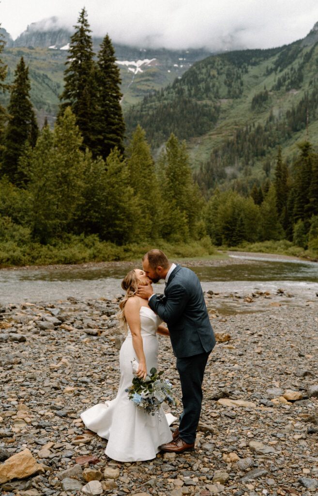 Bride and groom kissing near a river in Glacier National Park