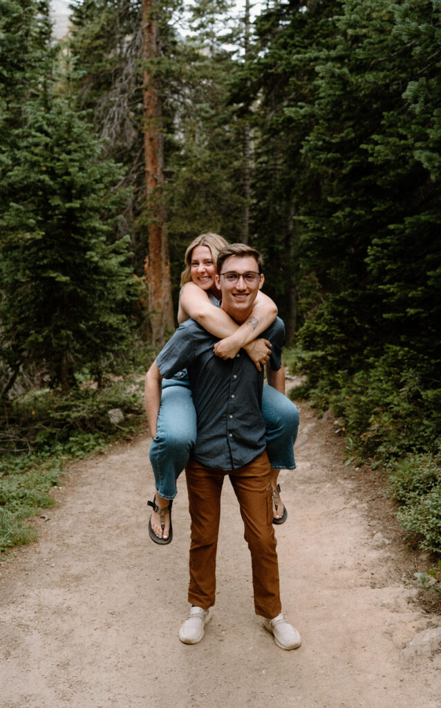 Fiancée on fiancés back during a hike at Lake Isabelle