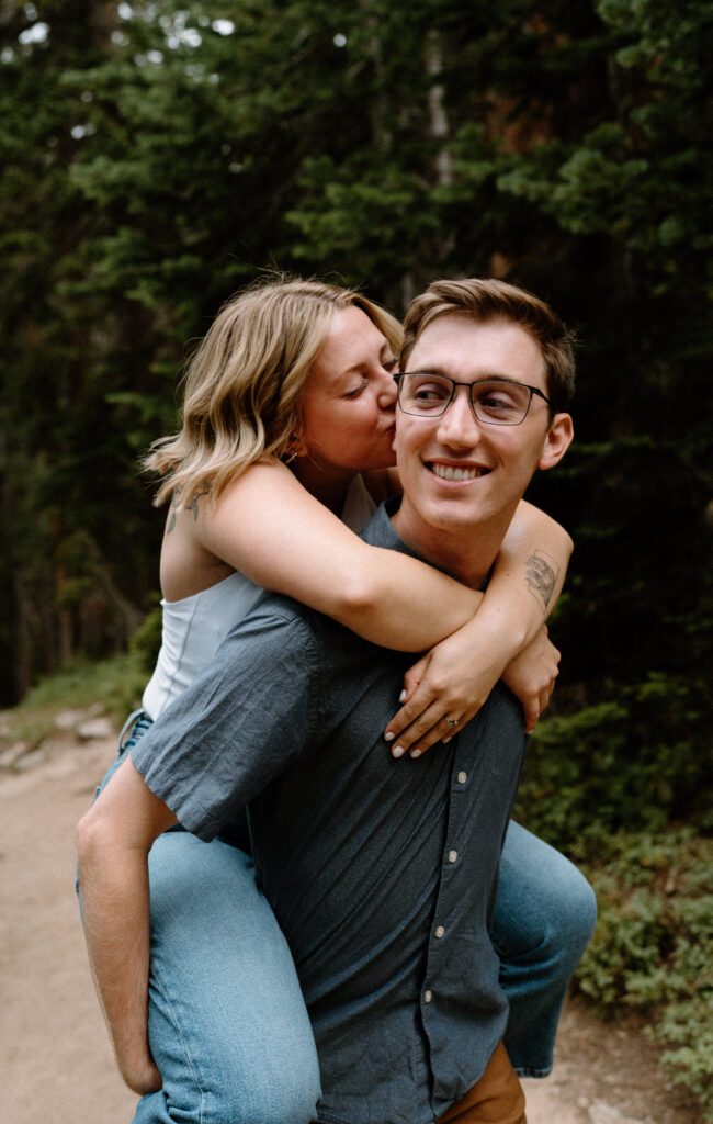 Fiancée kissing fiancé's cheek while on his back during an engagement session at Lake Isabelle