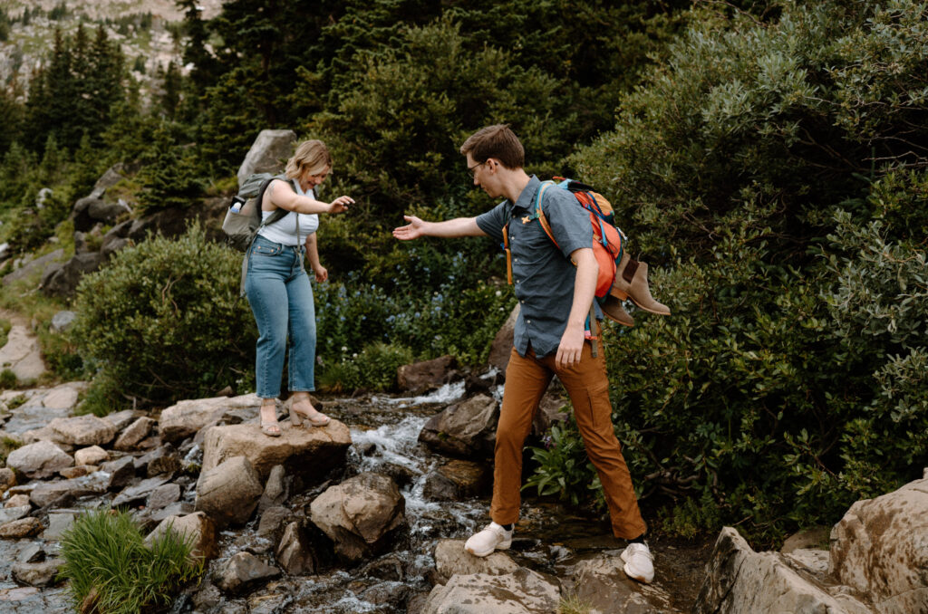 Couple hiking over a river during an engagement at Lake Isabelle