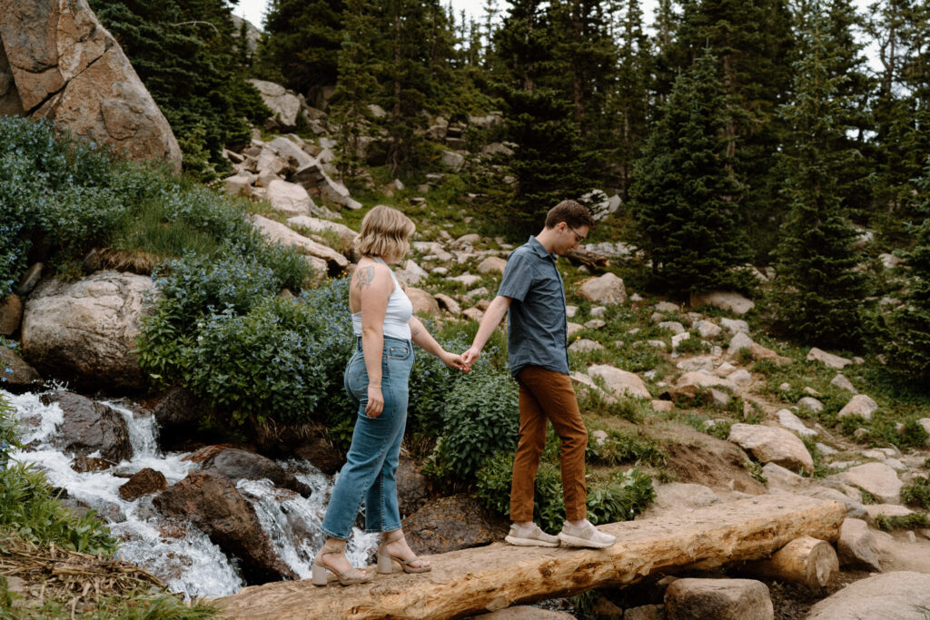 Couple walking over a bridge while hiking at Lake Isabelle during engagement session
