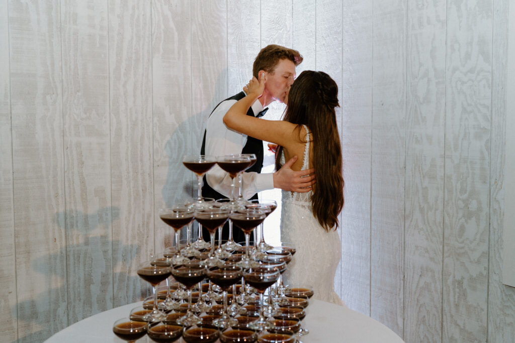 Bride and groom kissing in front of espresso martini tower on wedding day at Woodlands