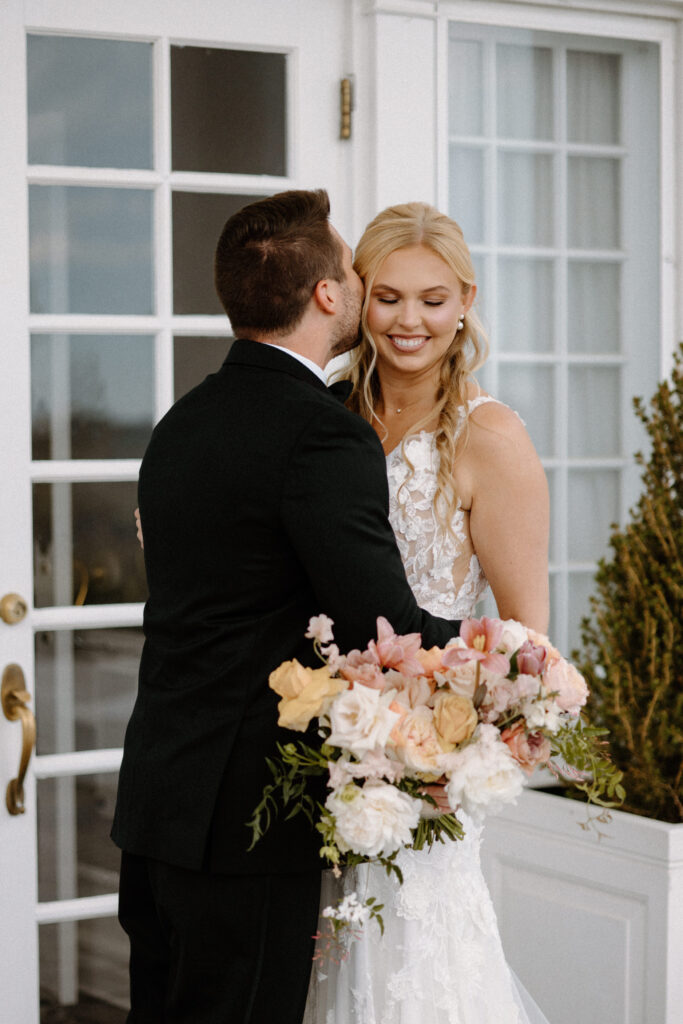 Groom kissing bride's cheek during first look at The Manor House