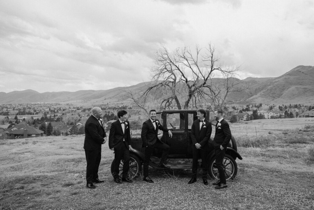 Groom and groomsmen smiling by an old car at The Manor House on wedding day