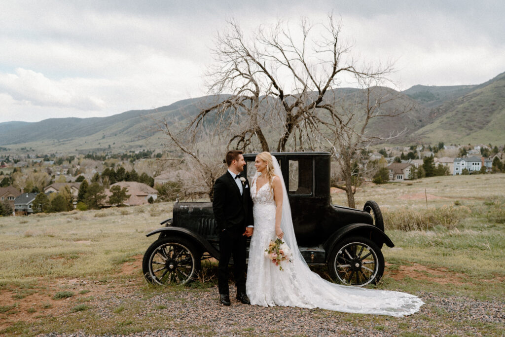 Bride and groom smiling in front of a classic car at Manor House